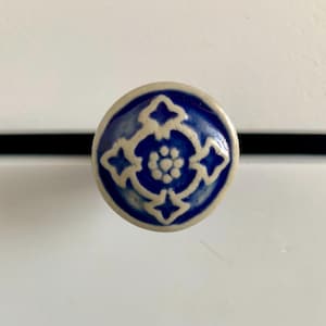 May include: A round ceramic cabinet knob with a blue and white floral design. The knob features a dark blue background with a white floral pattern in the center and around the edges. The knob is a decorative element.