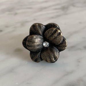 May include: A black metal flower-shaped cabinet knob with a clear rhinestone in the center.