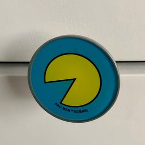 May include: A round, blue and yellow Pac-Man themed cabinet knob with the text "PAC-MAN TM & ©BNEI".
