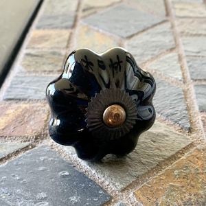 May include: Black ceramic cabinet knob with a decorative, scalloped edge and a gold-toned metal center.