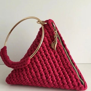 May include: A triangular crocheted handbag with a gold ring handle and a zipper closure. The bag is a vibrant crimson red color.