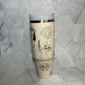 May include: A cream-colored stainless steel tumbler with a white lid. The tumbler features a silver outline of Stitch and other characters from Lilo & Stitch, including flowers and leaves.