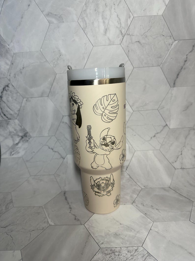 May include: A cream-colored stainless steel tumbler with a white lid. The tumbler features a silver outline of Stitch and other characters from Lilo & Stitch, including flowers and leaves.