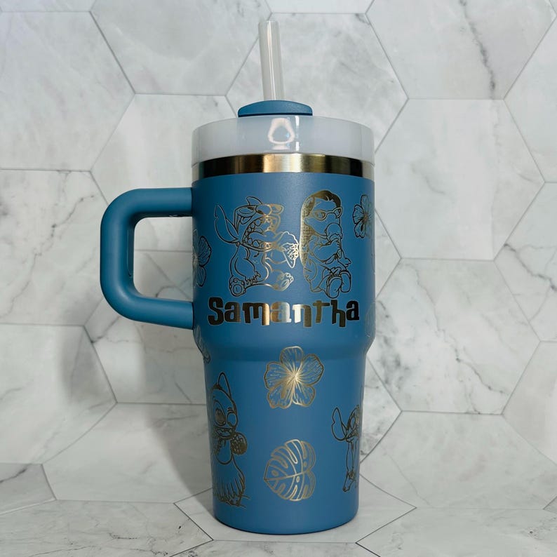 May include: A blue stainless steel travel mug with a handle and a straw. The mug has a gold design of Stitch and Angel from Lilo & Stitch, along with tropical flowers and leaves. The name "Samantha" is engraved on the mug.