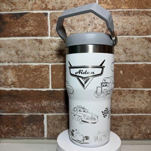 Puede incluir: Taza de viaje de acero inoxidable blanca con asa y tapa grises. La taza tiene un diseño en blanco y negro de coches de la película Cars. La taza está personalizada con el nombre "Aiden".