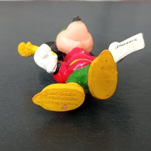 May include: A yellow, red, green, and white plastic Mickey Mouse figurine holding a paper with the word "Dear" written on it. The figurine is made by Walt Disney Productions and is made in Hong Kong.
