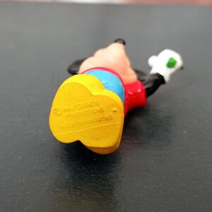 Puede incluir: Una figurita de pl&aacute;stico amarilla, roja y azul de Mickey Mouse. La figurita lleva una camisa roja, pantalones azules y zapatos amarillos. La figurita sostiene un objeto verde en su mano derecha. La parte inferior de la figurita tiene la informaci&oacute;n de copyright "&copy; Disney", "Made in China" y "Hong Kong".