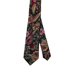 Op de afbeelding: Een zwarte stropdas met een herhalend patroon van vogels, bloemen en bladeren in tinten rood, roze, goud en blauwgroen. De stropdas is gemaakt van een geweven stof.