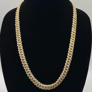 Könnte beinhalten: Eine goldene Halskette mit einem kubanischen Gliederketten-Design. Die Kette ist mit kleinen, klaren Steinen besetzt.
