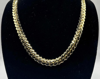 May include: A gold chain necklace with a curb link style. The chain is displayed on a black velvet mannequin bust.
