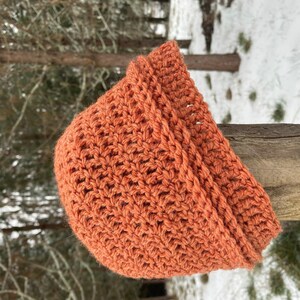 May include: A crocheted beanie in a warm orange color. The beanie is made with a textured stitch and has a folded brim.