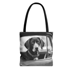 May include: Black and white photo of a dog looking out of a car window. The dog is wearing a collar and is sitting in the front seat of the car. The photo is printed on a tote bag.