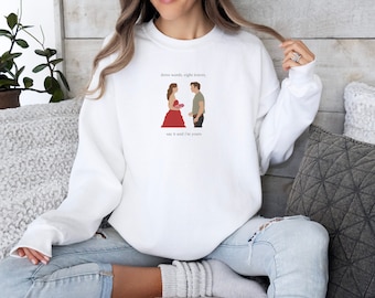 May include: White sweatshirt with a graphic of a couple and the text "three words, eight letters. say it and I'm yours."