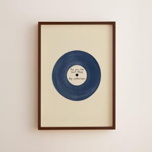 Könnte beinhalten: Gerahmter Kunstdruck mit einem marineblauen Vinyl-Schallplatten-Design. Die Schallplatte trägt den Text "You are the best thing" und "Ray LaMontagne". Das Kunstwerk ist vor einem cremefarbenen Hintergrund platziert und in einem dunkelbraunen Rahmen gerahmt.