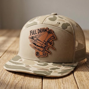 May include: A tan and beige camouflage trucker hat featuring a brown leather-like patch on the front. The patch displays a graphic of a compound bow and the text "FULL DRAW" in black lettering. The hat has a mesh back and a flat brim.