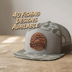 May include: A gray trucker hat with a camouflage pattern on the brim and back mesh panels. A circular leather patch on the front features a fish illustration and the text 'CHASING BROOKIES'. The text '40 FISHING DESIGNS AVAILABLE' appears above the hat.
