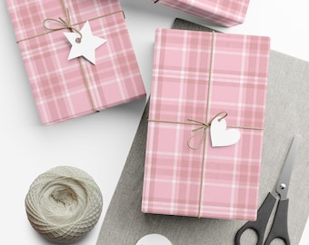 May include: Pink plaid-patterned gift boxes tied with twine and white tags. A spool of twine, scissors, and blank tags are also present. The gifts are wrapped in pink and white plaid paper.