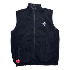 Puede incluir: Chaleco de vellón negro con cierre de cremallera y un logotipo de los Rams en la parte delantera. El chaleco tiene un parche rojo y blanco de "St. Louis" en la parte inferior izquierda.