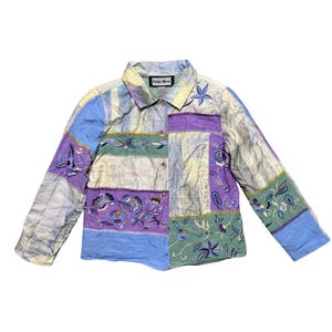 Könnte beinhalten: Ein mehrfarbiges, langärmliges Hemd mit Knöpfen, Patchwork-Muster und Blumenstickerei. Das Hemd ist aus leichtem Stoff gefertigt und hat eine lockere Passform. Das Etikett auf dem Hemd lautet "Indigo Moon".