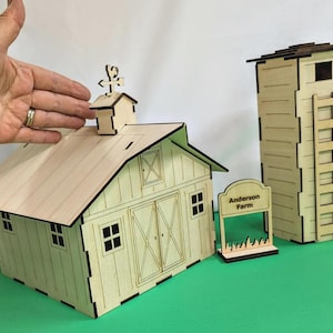 Puede incluir: Un conjunto de granja de madera con un granero, un silo y un letrero. El granero tiene un tejado a dos aguas, puertas dobles y pequeñas ventanas. El silo tiene un diseño de escalera. El letrero dice "Anderson Farm". El conjunto es de madera clara.