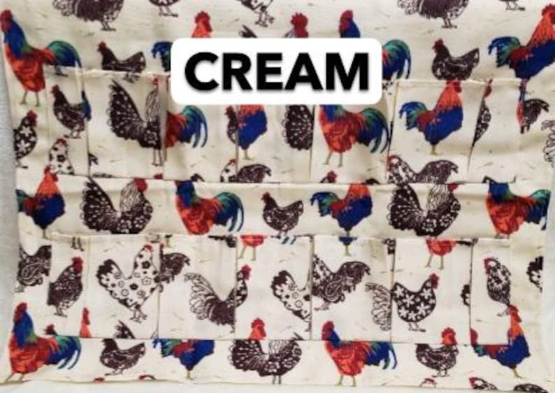 May include: Cream-colored fabric organizer with multiple pockets, featuring a repeating pattern of roosters and hens in red, blue, and black. The word "CREAM" is displayed in a white rectangular box.