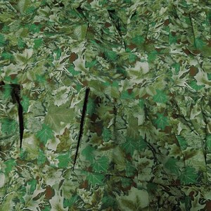 May include: Close-up of a fabric with a camouflage pattern. The design features a dense arrangement of green, brown, and white leaf shapes. The fabric appears to be pleated or gathered, creating a textured surface.