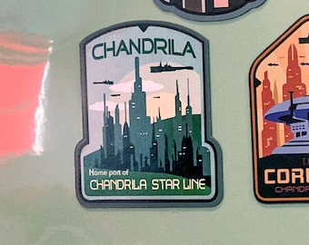 Könnte beinhalten: Ein grüner, blauer und weißer Patch mit dem Text "CHANDRILA" und "CHANDRILA STAR LINE" mit einer Skyline aus hohen Gebäuden im Hintergrund.