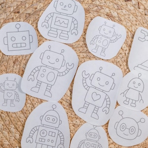 May include: A collection of white fabric patches featuring various robot designs outlined in gray stitching. The robots have different shapes and expressions, some with hearts or waving arms. The patches are arranged on a woven surface.