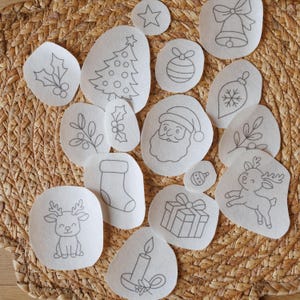 May include: A collection of white felt Christmas-themed cutouts with black outline drawings. Designs include a Christmas tree, Santa Claus, reindeer, ornaments, a bell, a gift, a candle, and holly.