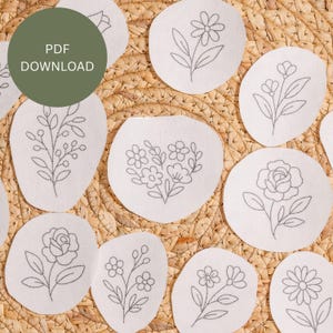 May include: Several white, oval fabric patches with grey embroidered floral designs. The patches display different flower types, such as roses and daisies. A green circle with the text "PDF DOWNLOAD" is in the upper left corner. The patches are arranged on a woven surface.