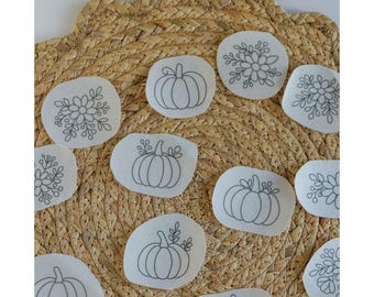 May include: The image shows several white fabric patches with black line drawings of pumpkins and floral designs. The patches are arranged on a woven, beige placemat. The text "Stick and Stitch" is at the top of the image.