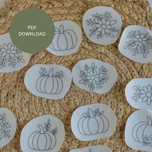 May include: A collection of white fabric patches with black embroidered designs of pumpkins and floral patterns. The patches are arranged on a woven, light brown surface. A green circle with the text "PDF DOWNLOAD" is in the upper left.