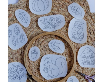 May include: A collection of pre-printed embroidery designs featuring autumn-themed images like a pumpkin, leaves, an owl, and a squirrel. The designs are on oval-shaped fabric pieces, with a wooden embroidery hoop and scissors. The text "Stick and Stitch" is at the top.