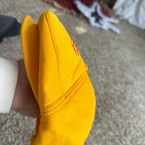 May include: A bright yellow baseball cap with a curved brim. The cap has red lettering on the front. The hat is made of a soft material and has a structured design.