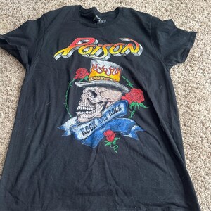 May include: Black t-shirt featuring the word "Poison" in a stylized font above a skull wearing a top hat and surrounded by roses. A banner below the skull reads "Rock and Roll".