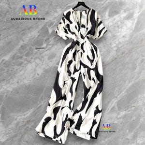 Puede incluir: Mono con estampado en blanco y negro, cuello en V y mangas cortas, colgado de una percha negra. El mono presenta un diseño abstracto y audaz. La marca "Audacious Brand" es visible en las esquinas.