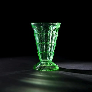 Può includere: Un vaso di vetro verde con un design a scanalature. Il vaso è alto e stretto con una base svasata.