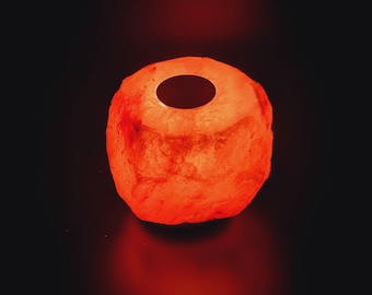 Könnte beinhalten: Eine runde, orangefarbene Himalaya-Salzlampe mit einem kleinen Loch oben. Die Lampe ist eingeschaltet und leuchtet.