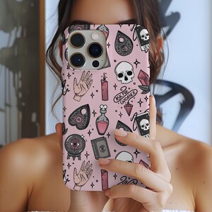Puede incluir: Funda de teléfono rosa con un patrón repetido de símbolos ocultos, incluyendo calaveras, manos, velas y botellas de pociones. La funda también tiene el texto "ASK FOR GUIDANCE".