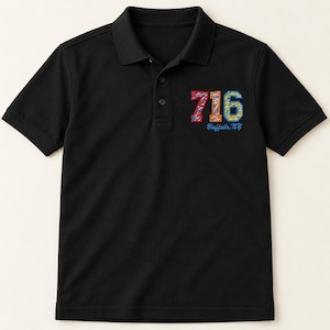 May include: A black short-sleeved polo shirt with a collar and three buttons. The chest features an embroidered graphic with the number 716 in red, orange, and blue, with the text Buffalo, NY written in blue script underneath the numbers.