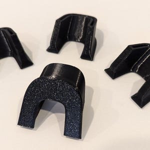 May include: Four black plastic U-shaped pieces, possibly for a 3D printer or other project.