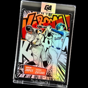 May include: Baseball trading card featuring comic book style illustrations of Aaron Judge and Shohei Ohtani. The card is encased in a protective holder with the word "V-BOOM" in the background.