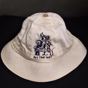 May include: White bucket hat with a wide brim. The hat features a navy blue graphic of a cartoon character and the text "L.B.S. ALL THE WAY". A small, round button is on top of the hat.