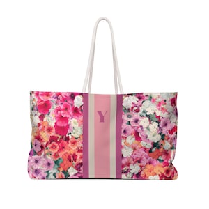 Könnte beinhalten: Eine große Tragetasche mit einem lebendigen Blumenmuster in Rosa, Rot, Orange und Weiß. Die Tasche hat einen vertikalen Streifen mit dem Buchstaben "Y" in der Mitte und weiße Seilgriffe.
