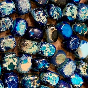 May include: A close-up of a collection of blue and white jasper tumbled stones. The stones are smooth and polished, with a variety of patterns and colors.