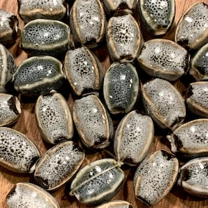 May include: A collection of oval-shaped ceramic beads with a speckled white and gray glaze. The beads have a rustic, handmade look and are perfect for jewelry making or crafting.