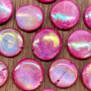 May include: A collection of iridescent pink and gold round beads with a pearlescent finish. The beads are approximately 1 inch in diameter.