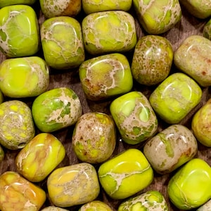 May include: A collection of tumbled green and brown jasper stones. The stones are smooth and polished, with a variety of patterns and textures.