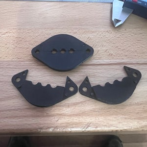 May include: Three black plastic parts for a 3D printed project. The parts are shaped like a circle with a hole in the middle and two curved pieces with teeth.