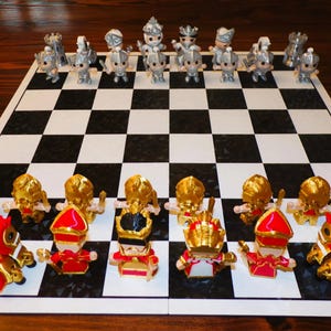 May include: A chessboard with gold and silver chess pieces. The gold pieces are on the bottom half of the board and the silver pieces are on the top half of the board.